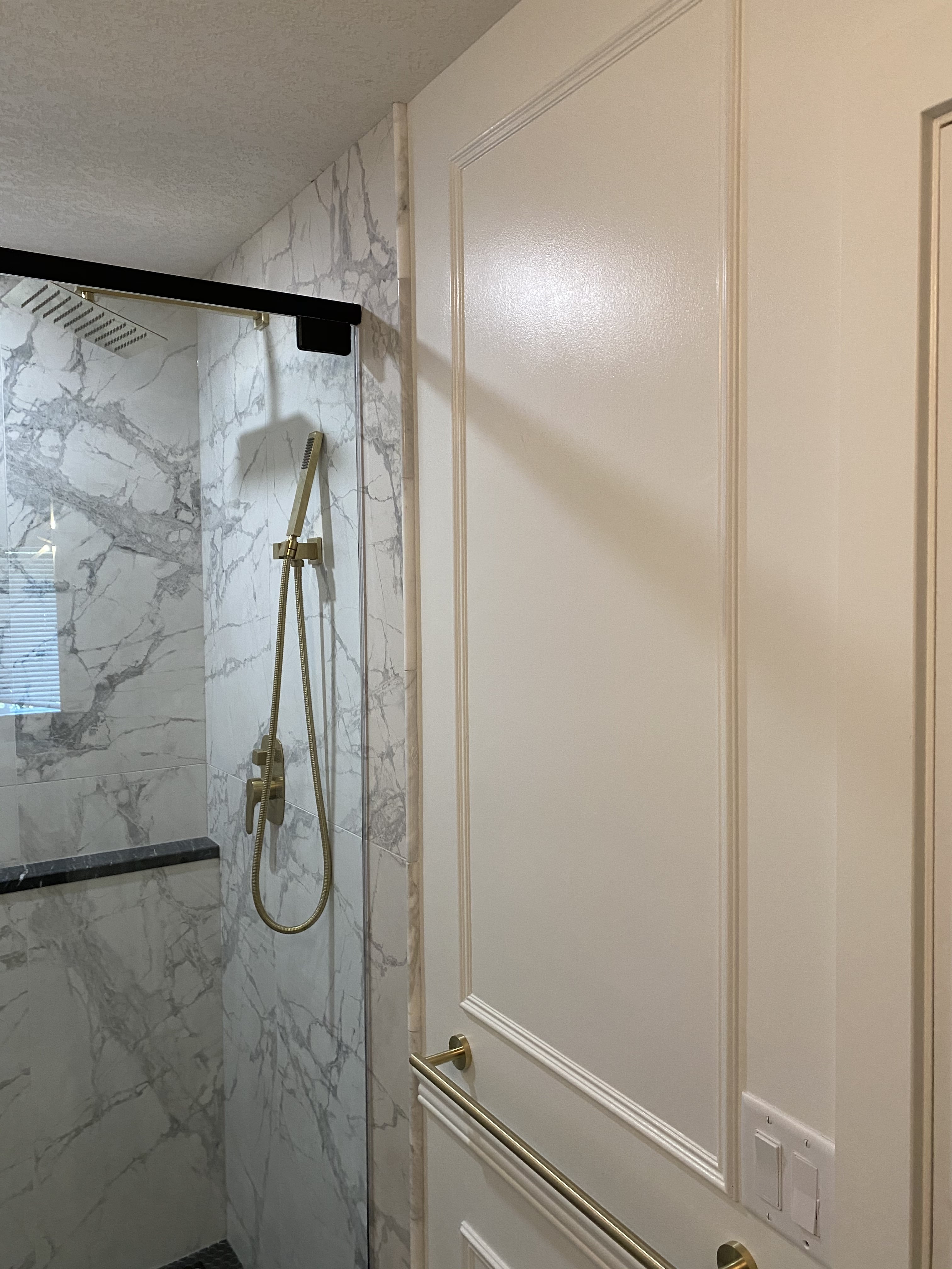 The shower includes a black granite shampoo ledge and curb with a hinged glass door.
